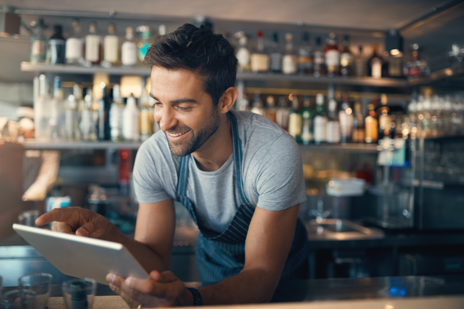 Shot of a young man using a digital tablet while working behind a bar counter